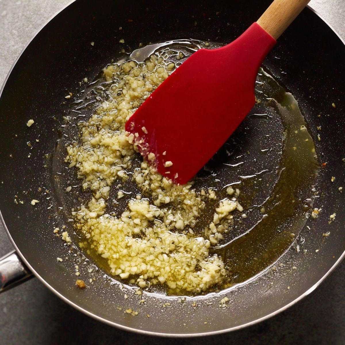 The Best Creamy Salmon Pasta Recipe 11 "Minced garlic sautéing in melted butter in a pan with a red spatula."
