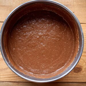 A round cake pan filled with chocolate batter, smoothed out for even baking.