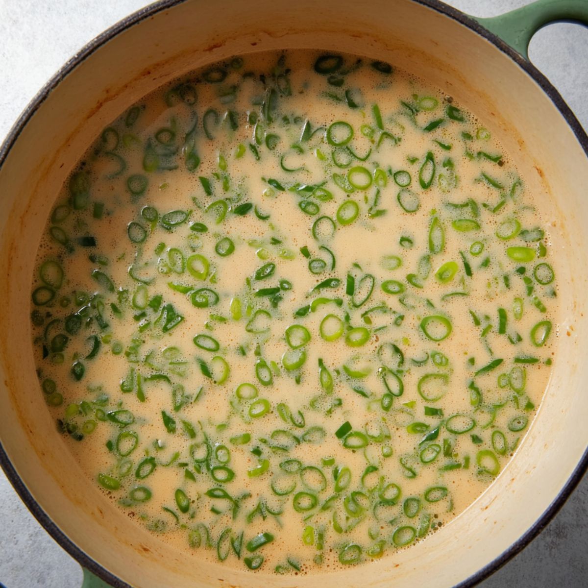 Best Ginger Miso Brothy Soup Recipe 13 A Dutch oven containing creamy miso-ginger broth with finely sliced green onions floating evenly across the surface. The broth has a light beige color and looks rich and aromatic, indicating a finished or nearly finished soup base.