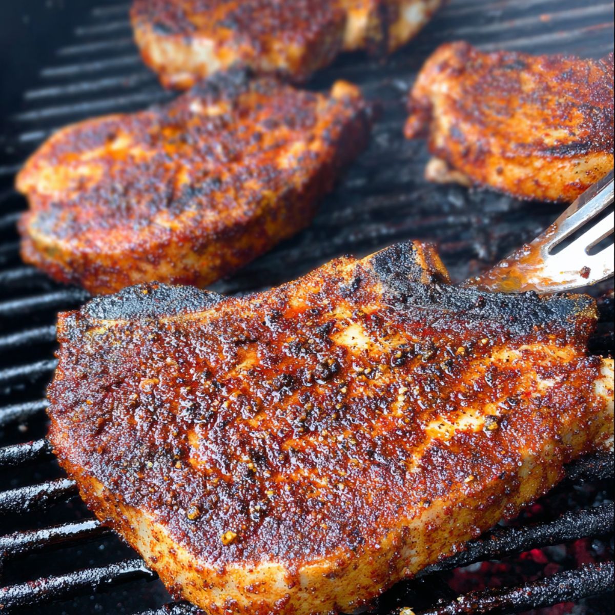 Easy Grilled Spiced Pork Chops Recipe 13 Close-up of four pork chops on a grill, seared with a darkened, caramelized crust, showing the texture of the spice rub and lightly charred edges.