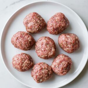 Best Homemade Kotleti Recipe 16 A white plate holding uncooked meatballs, evenly spaced, showing the texture of the ground meat mixture.