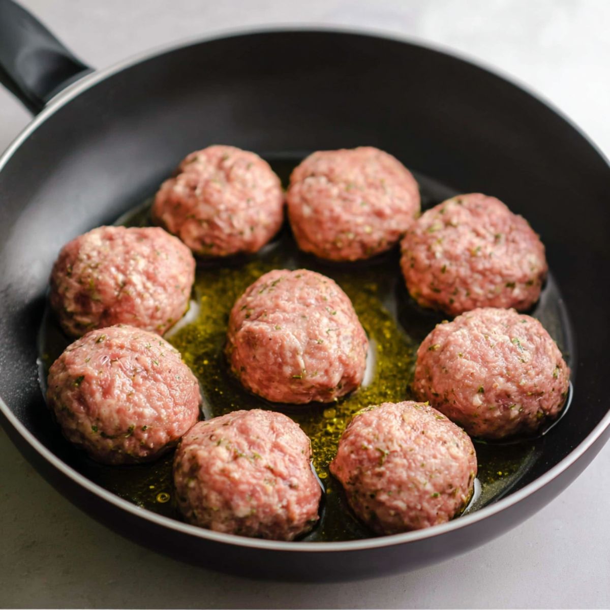 Best Homemade Kotleti Recipe 12 Raw, uncooked meatballs arranged in a frying pan with a small amount of oil, ready to be cooked.