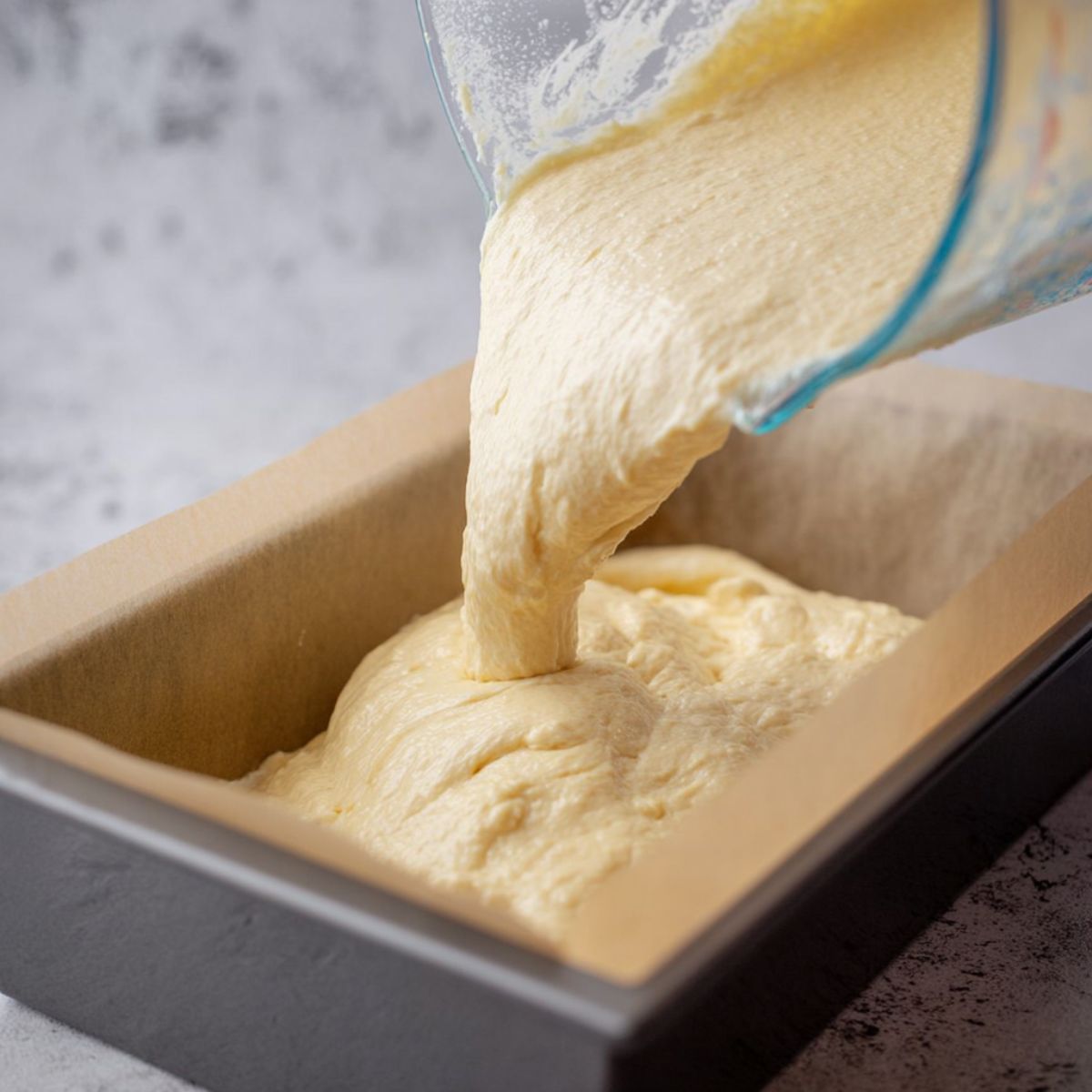 Healthy Lemon Buttermilk Cake Recipe 11 Thick cake batter being poured from a glass measuring cup into a lined baking pan.