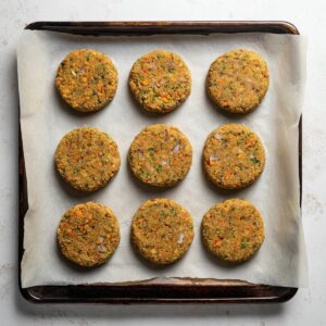 Delicious Lentil Patties Recipe 16 Nine uncooked lentil and vegetable patties arranged in a grid on a parchment-lined baking sheet, ready to bake.