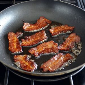Easy Monterey Chicken Skillet Recipe 15 A frying pan with crispy, browned bacon slices cooking in their rendered grease.