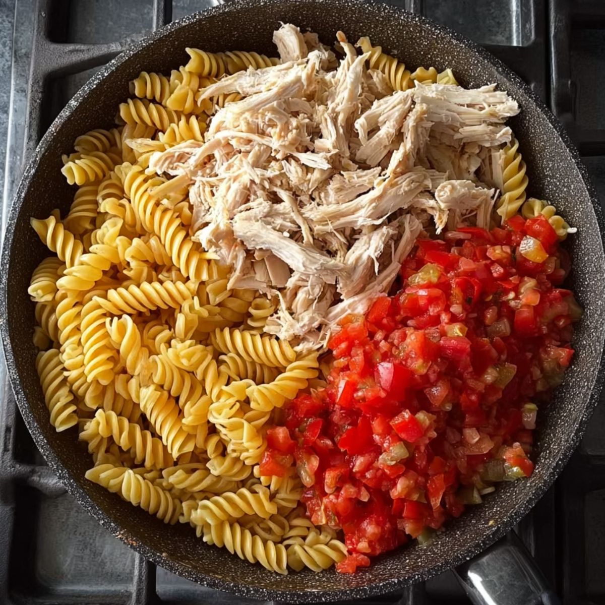Easy Monterey Chicken Skillet Recipe 10 A skillet with uncooked rotini pasta, shredded chicken, and diced tomatoes, showing ingredients before mixing.