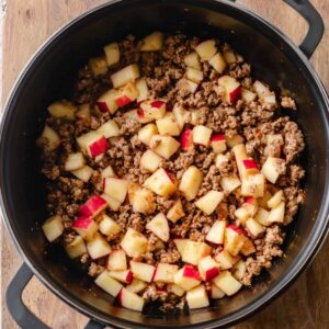 Easy Olive Garden Zuppa Toscana Soup Recipe 16 Black pot with cooked ground meat and diced red-skinned potatoes mixed together, ready to simmer in the soup.
