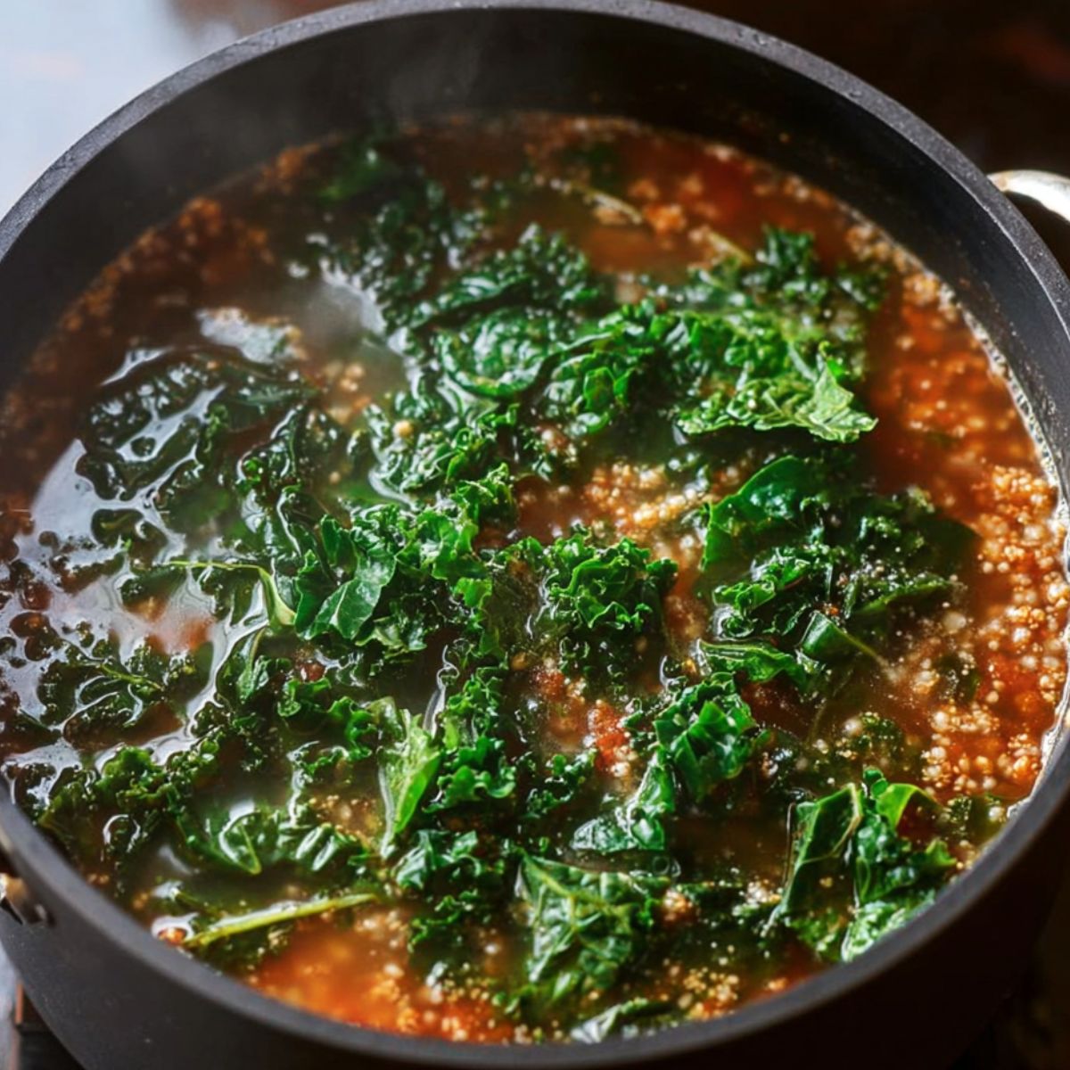 Easy Olive Garden Zuppa Toscana Soup Recipe 13 Black pot filled with simmering soup, containing chopped kale floating on top of a tomato-based broth with grains or lentils.