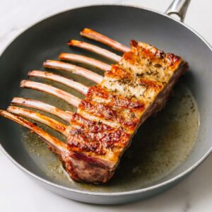 The Best Pan-Seared Lamb Chops Recipe 15 A gray skillet containing a whole rack of lamb, seared on top with a golden brown crust, ready for finishing in the oven.