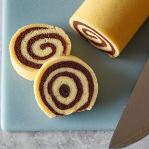 The Best Pinwheel Cookies Recipe 16 Two pinwheel cookies sliced from a rolled dough log, showing spiral chocolate-and-vanilla pattern.