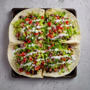 Healthy Sheet Pan Crunchwrap Recipe 15 A close-up shot of a large tortilla filled with a vibrant mix of fresh ingredients including lettuce, diced tomatoes, red onions, and sour cream. The veggies are neatly placed over the tortilla, making it look fresh and appetizing