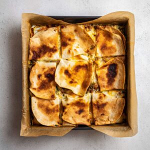 Healthy Sheet Pan Crunchwrap Recipe 16 A crispy and golden-brown sheet pan crunchwrap cut into neat squares, with perfectly melted cheese and a well-cooked filling, all served on parchment paper. The edges are perfectly crisp and browned, making it an inviting dish for a family meal