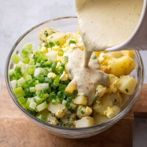 Healthy Southern Potato Salad Recipe 18 Pouring a smooth and flavorful dressing over freshly boiled potatoes, celery, eggs, and green onions for a classic potato salad.