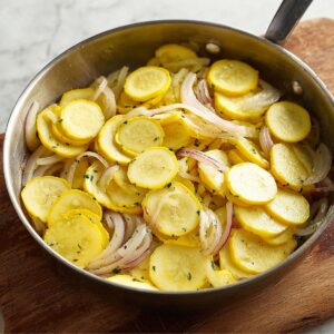 Best Squash Casserole Recipe 16 Sliced yellow squash added to the skillet with sautéed onions, creating a colorful and fresh layer of vegetables.