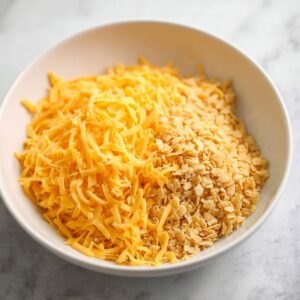 Best Squash Casserole Recipe 18 A close-up of a bowl of shredded cheddar cheese and crushed crackers, prepared to be sprinkled over the casserole for a crunchy topping.