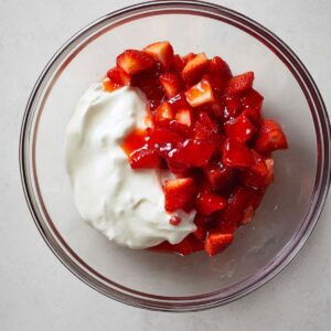Healthy Strawberry Yogurt Clusters Recipe 13 Top-down view of a glass bowl with diced strawberries blended into creamy pink yogurt, ready for freezing into popsicles, bright lighting.