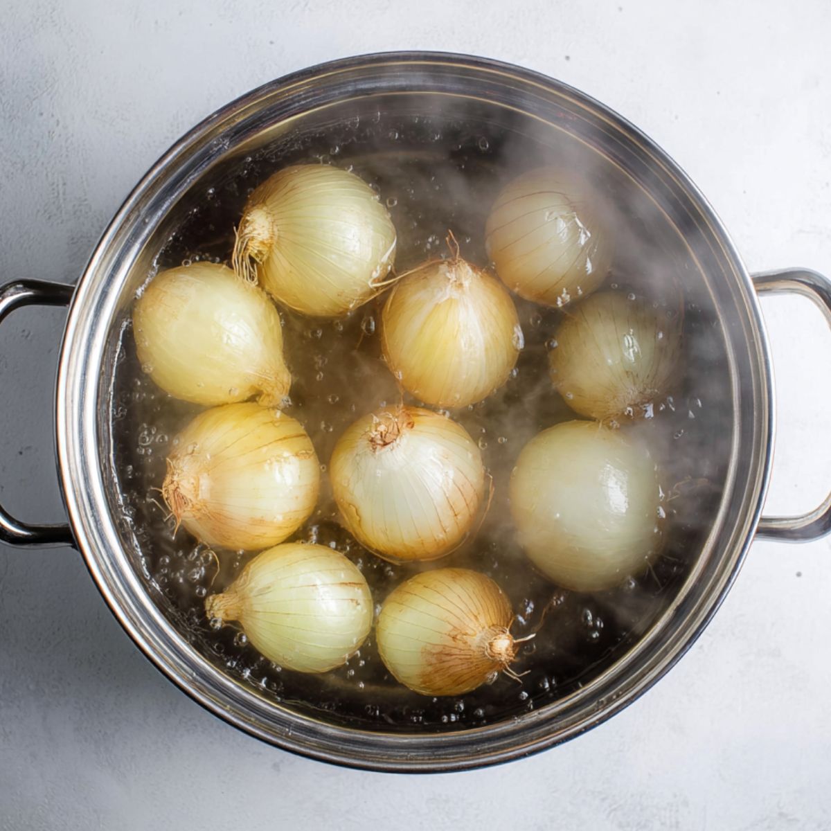 Delicious Stuffed Onions Recipe 10 A stainless steel pot filled with whole onions submerged in water, steaming gently. The onions are boiling, preparing to soften for the next step of cooking.