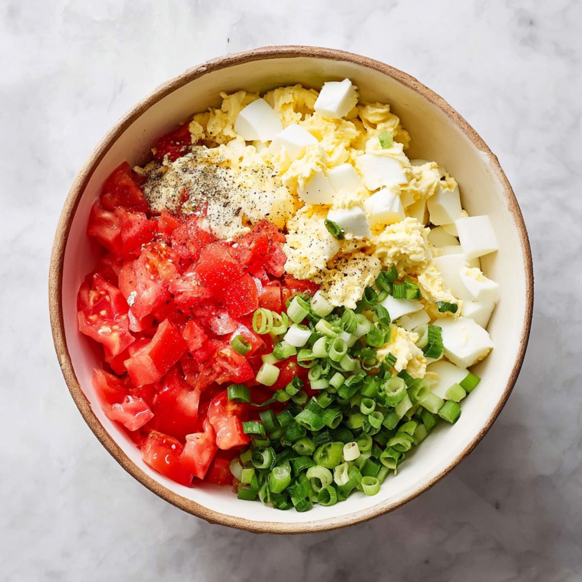Healthy Tomato Cracker Salad Recipe 11 A bowl filled with diced tomatoes, chopped boiled eggs, green onions, and mayonnaise, seasoned with salt and pepper, ready to be mixed into a fresh salad.