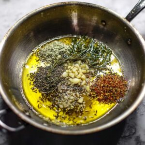 Easy Tomato Herb Soup Recipe 14 A pan with garlic and various dried herbs in olive oil, sizzling and preparing for a flavorful addition to a soup base.