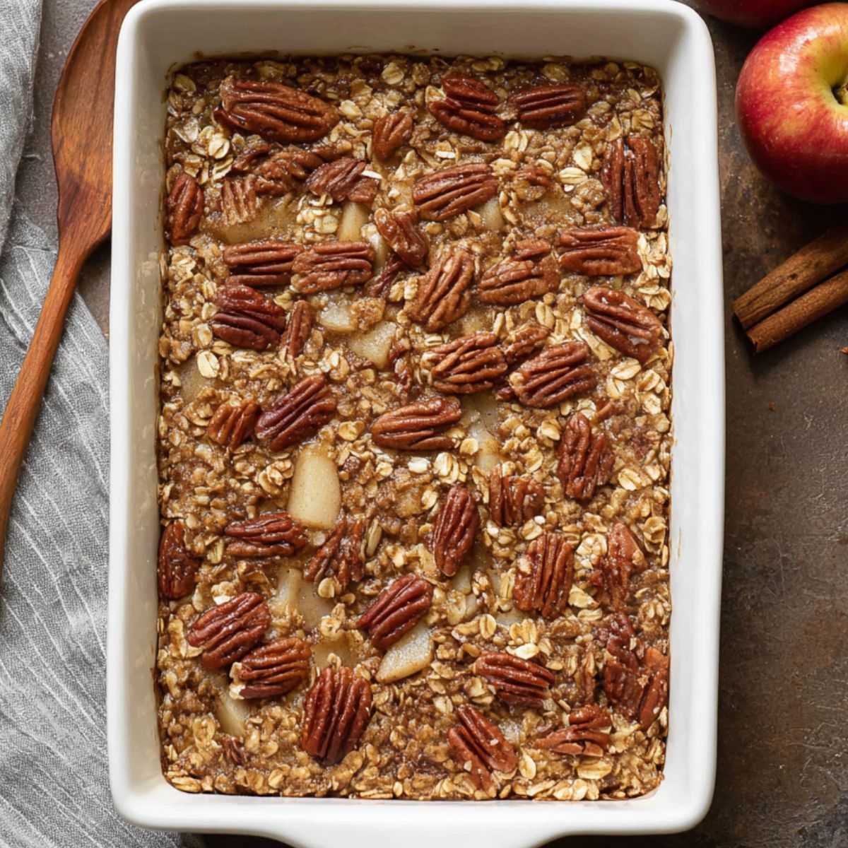 Best Baked Apple Oatmeal Recipe 13 A rectangular baking dish filled with baked apple oatmeal topped with whole pecans and oats, fresh from the oven.