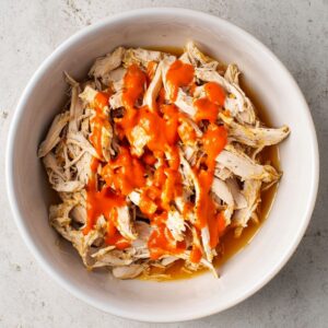 Best Buffalo Chicken Flatbreads Recipe 14 A bowl of shredded cooked chicken drizzled with bright orange buffalo sauce, ready to be added to flatbreads.