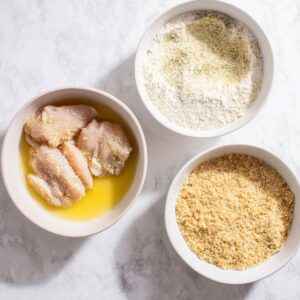 Chicken breast coated in breadcrumbs is being shallow fried in a pan of hot oil until golden and crispy.