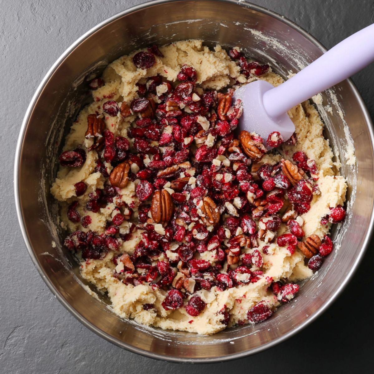 Best Cranberry Cookies Recipe 12 A mixing bowl filled with a cookie dough mixture, featuring chopped cranberries and pecans scattered inside, ready to be stirred together to form delicious cookie dough.