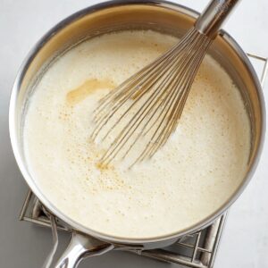 Delicious Creamy Grits Recipe 15 A stainless steel saucepan with a whisk inside, mixing light, frothy grits on a stovetop, capturing the preparation stage.