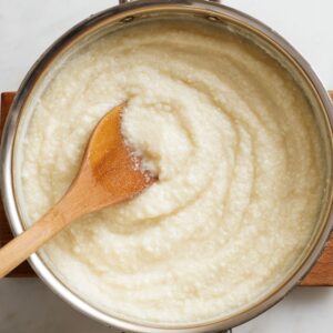 Delicious Creamy Grits Recipe 16 A saucepan filled with creamy, cooked grits being stirred with a wooden spoon, showing a smooth, thick texture.