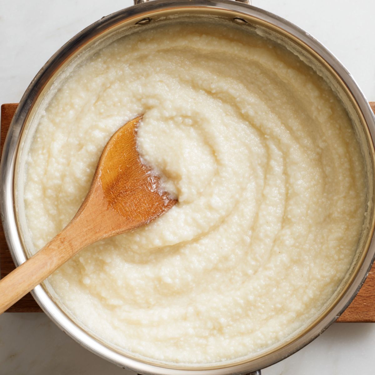 Delicious Creamy Grits Recipe 12 A saucepan filled with creamy, cooked grits being stirred with a wooden spoon, showing a smooth, thick texture.