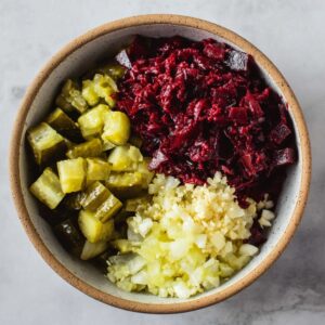 Delicious Grated Beet Salad Recipe 15 The ingredients for the salad separated in a bowl: diced pickles, grated beets, and minced garlic, ready to be mixed.