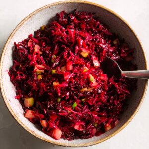 Delicious Grated Beet Salad Recipe 16 A bowl filled with finely shredded or grated beets mixed with small diced vegetables like pickles or apples. The salad has a deep red color from the beets, and a spoon is partially visible in the bowl.