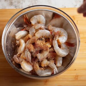 Easy Peri Peri Shrimp Recipe 14 Raw shrimp in a mixing bowl being seasoned with spices, ready to be cooked.