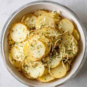 The Best Potato Galette Recipe 16 Bowl of thinly sliced potatoes seasoned with herbs and cheese, ready to be layered.