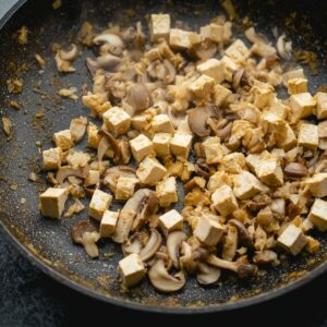 Best Saucy Ramen Noodles Recipe 17 Chopped mushrooms and tofu cubes being sautéed in a pan, preparing the filling for vegan ramen.