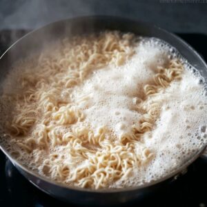 Best Saucy Ramen Noodles Recipe 16 Ramen noodles boiling in a pot of water, with foam forming on the surface as they cook.