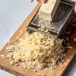Healthy Shredded Tofu Wraps Recipe 15 A hand grating a block of firm tofu on a box grater over a cutting board, creating shredded tofu pieces.